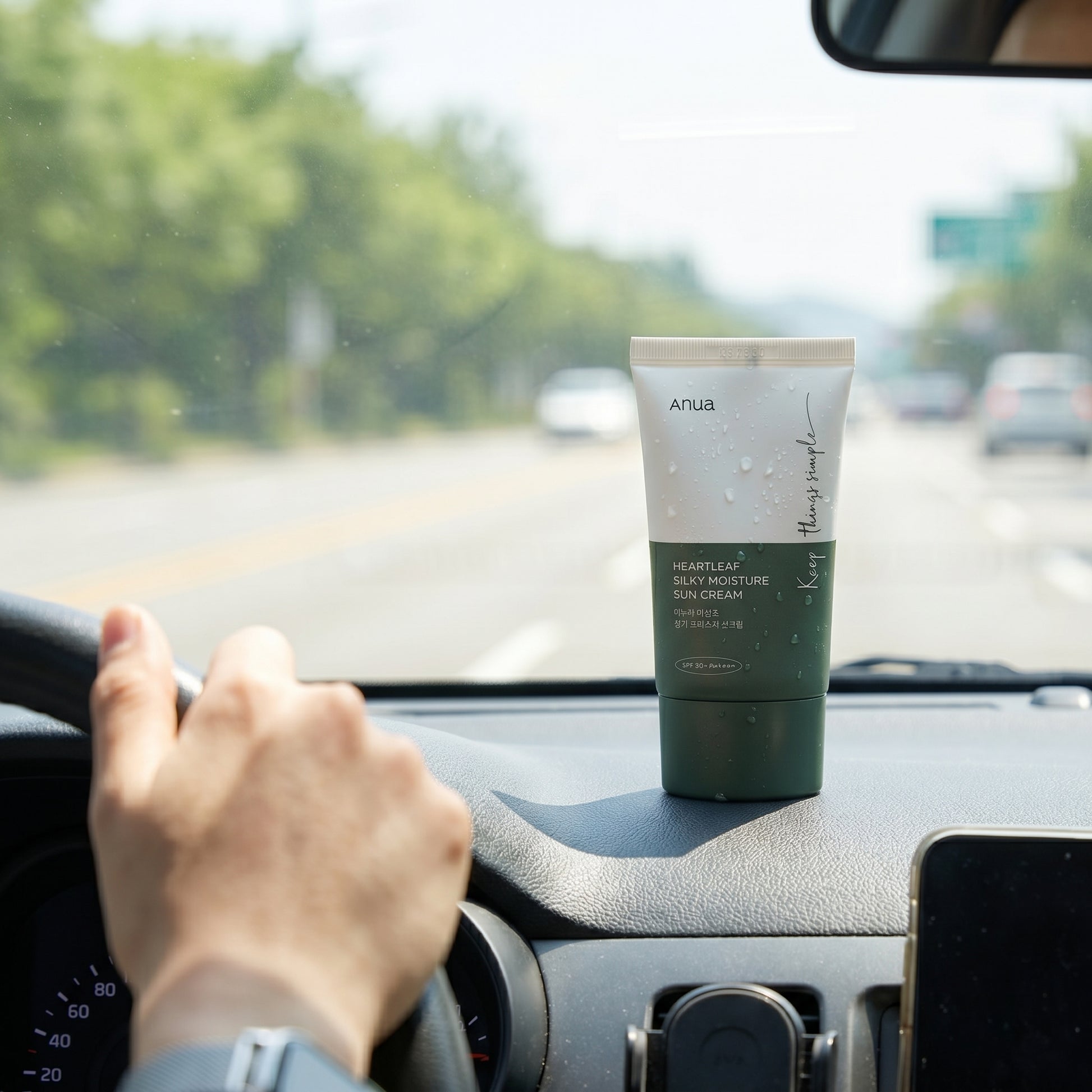 Tube of ANUA skincare product on a car dashboard with a hand on the steering wheel