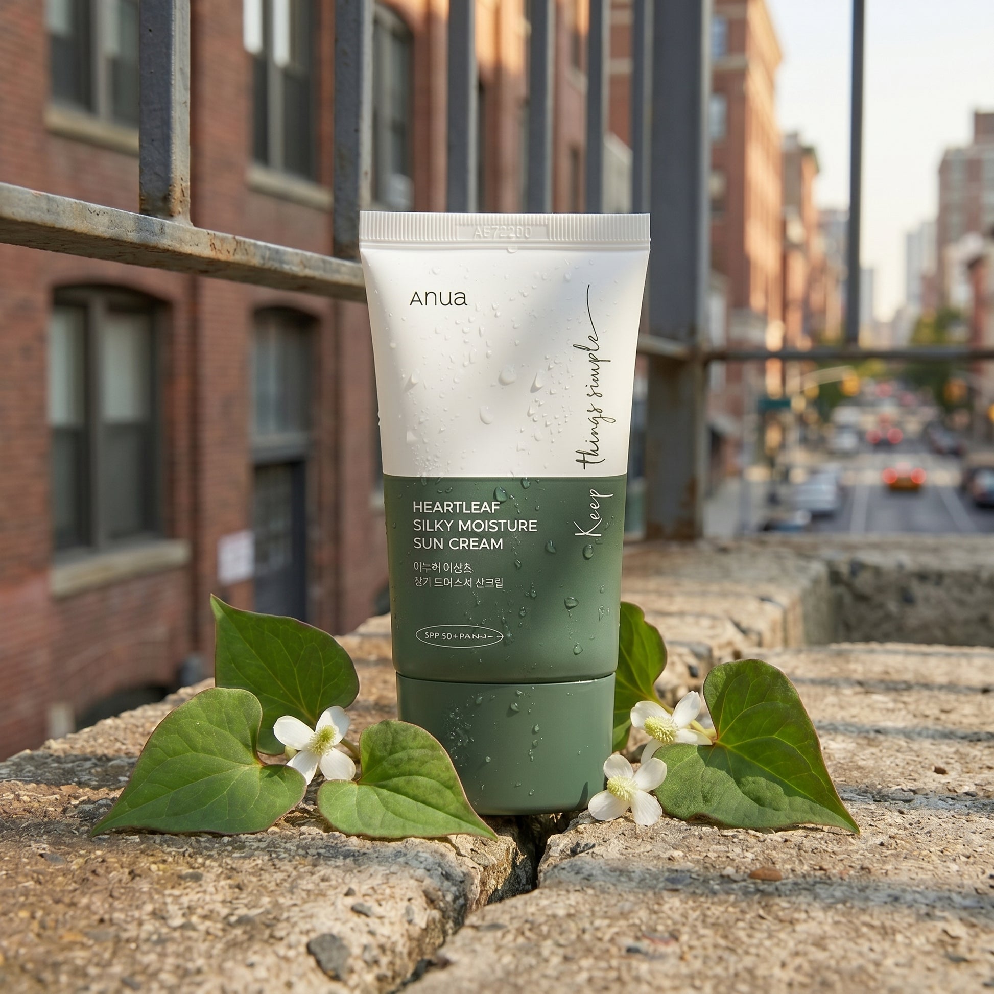 Tube of Anua sunscreen with green leaves and white flowers on a concrete ledge with urban background